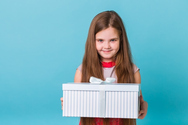 Niña sonriente con caja de regalo sobre pared azul.