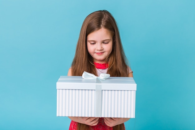 Niña sonriente con caja de regalo sobre pared azul.