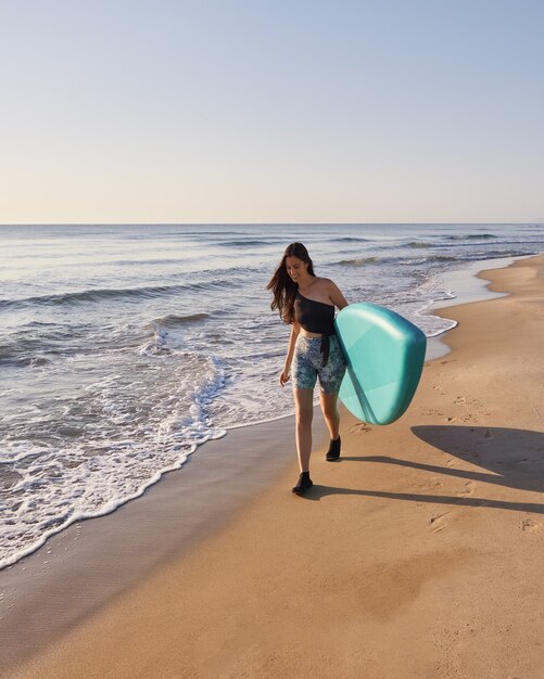 Niña sonriente caminando por la costa con una tabla de remo