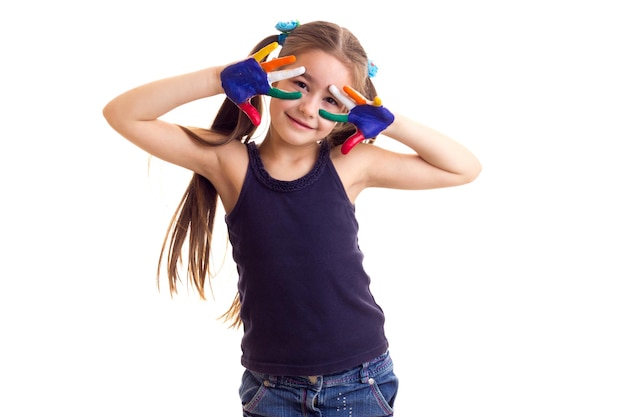 Niña sonriente con camisa negra y jeans con dos colas de caballo y manos de colores en el estudio