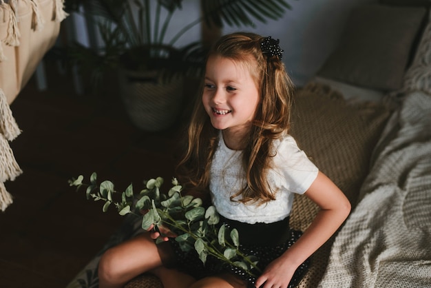 Niña sonriente en una camiseta blanca con una ramita verde de eucalipto en sus manos