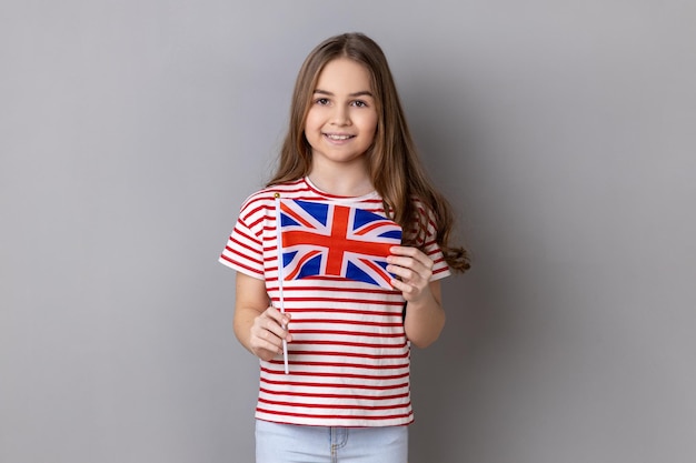 Niña sonriente con camiseta a rayas sosteniendo la bandera del Reino Unido mirando a la cámara