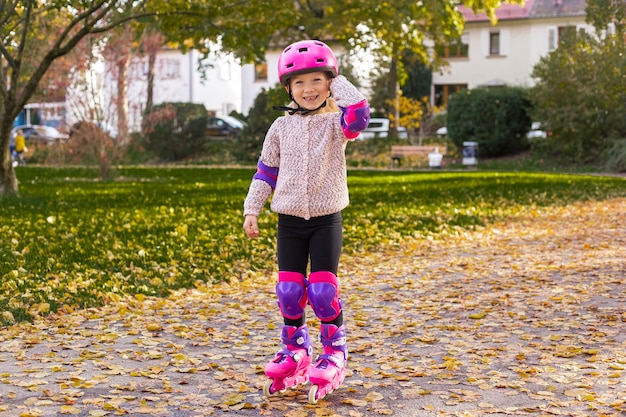 Niña sonriente en un casco en patines de protección en el parque