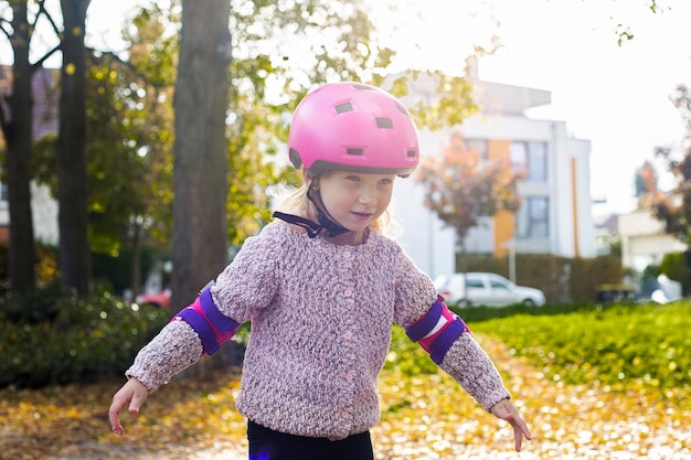 Niña sonriente en un casco en patines de protección en el parque