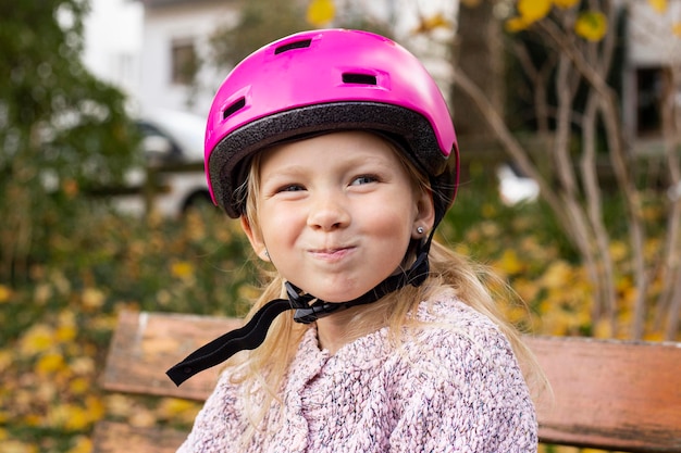 Foto niña sonriente con casco rosa sentada en un banco del parque