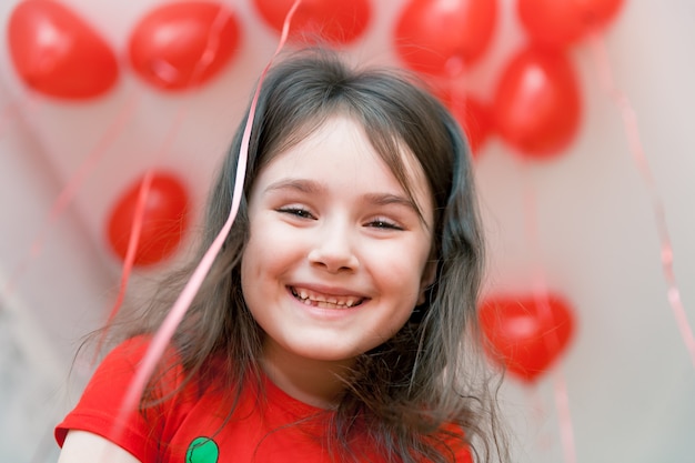 Niña sonriente cerca retrato con globos rojos sobre un fondo