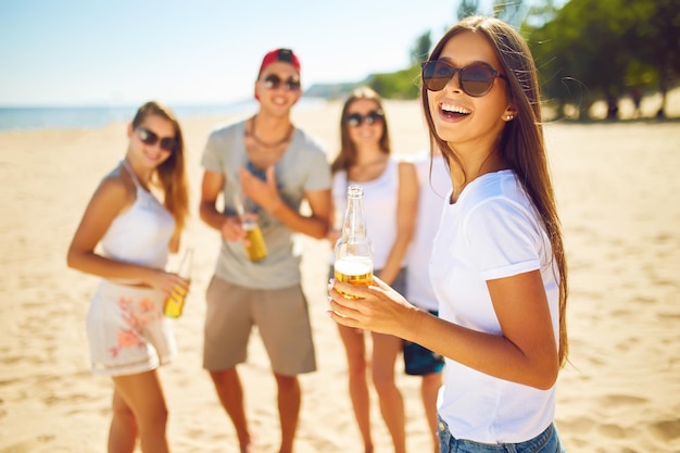 Niña sonriente con cerveza mientras la gente hace barbacoas en el fondo Diversión en la playa