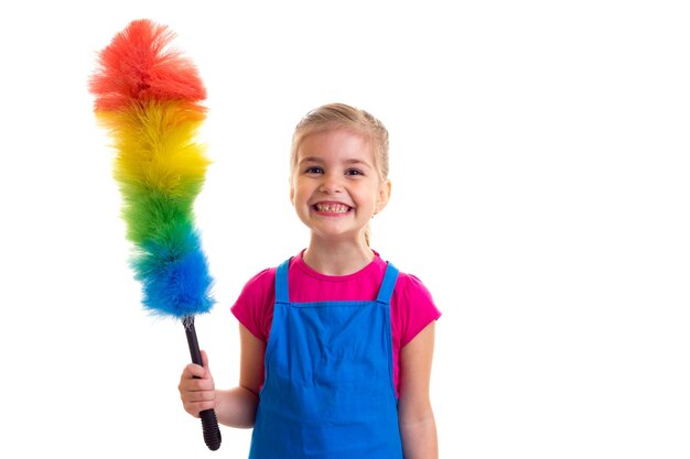 Niña sonriente con cola de caballo con camisa rosa y delantal azul con plumero de color en estudio