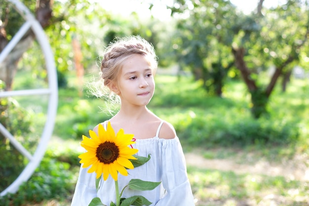 Niña sonriente con una coleta en la cabeza sostiene girasol en el jardín Niño con girasol