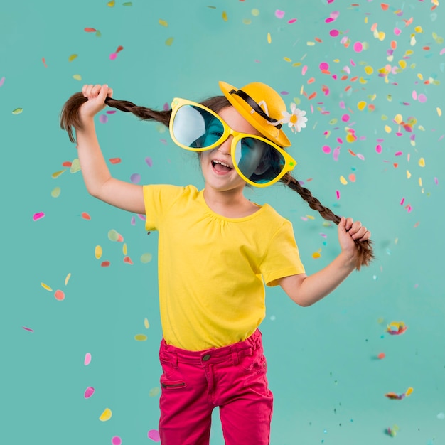 Foto niña sonriente con confeti y grandes gafas de sol