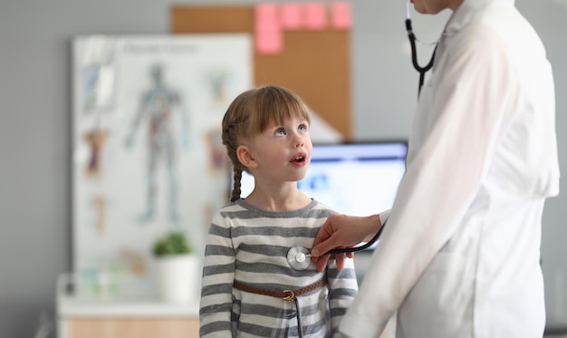 Niña sonriente en el consultorio médico en la clínica Pediatra examinando a un niño pequeño con un estetoscopio