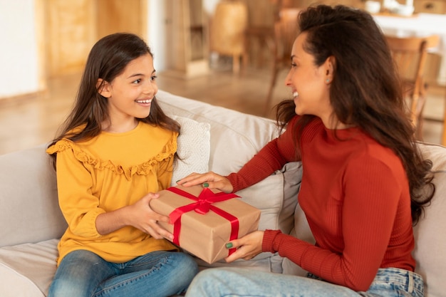 Niña sonriente dando regalo de cumpleaños a mamá en casa