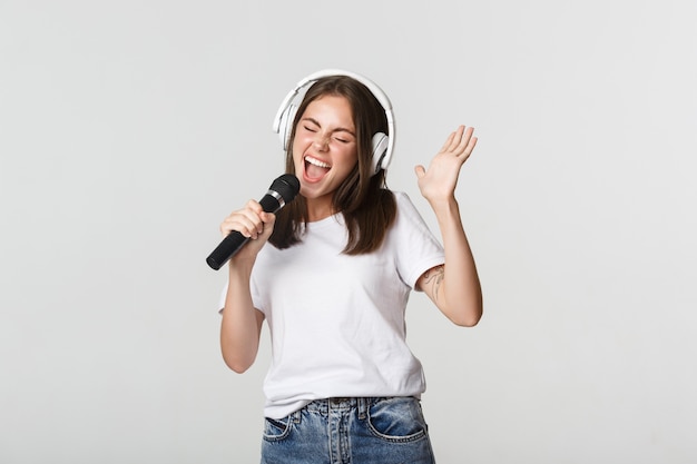 Niña sonriente despreocupada jugando karaoke, cantando en micrófono con auriculares