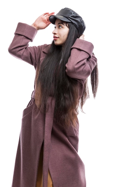 Niña sonriente con un elegante abrigo de otoño color vino y una gorra de cuero negro Bonita morena con el pelo largo Paseos cómodos en la estación fría Aislado en un fondo blanco Vertical