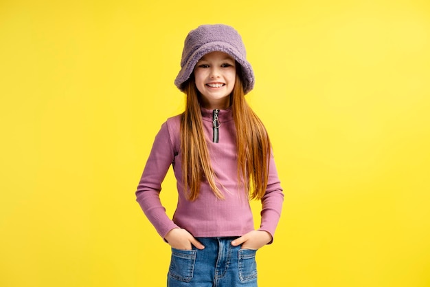 Foto niña sonriente con un elegante sombrero púrpura y ropa casual mirando el modelo de la cámara posando