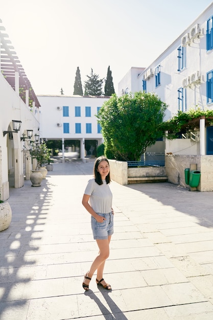 Niña sonriente se encuentra en el patio de una casa con arbustos verdes árboles y plantas en macetas