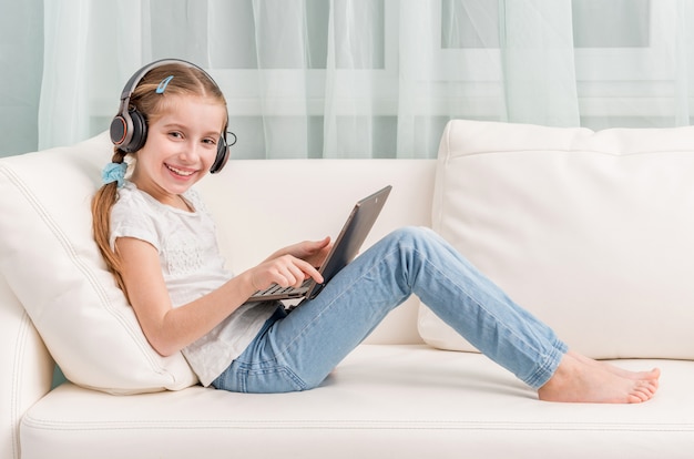 Niña sonriente escuchando algo con auriculares mira a la cámara