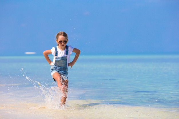 La niña sonriente feliz adorable se divierte en vacaciones de la playa