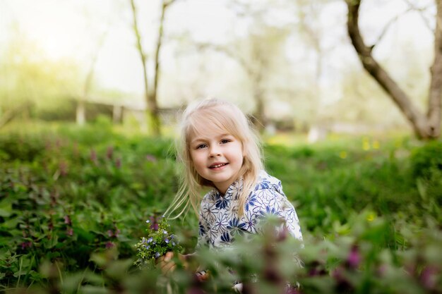 Niña sonriente con flores de primavera en el césped verde en el jardín foto de alta calidad