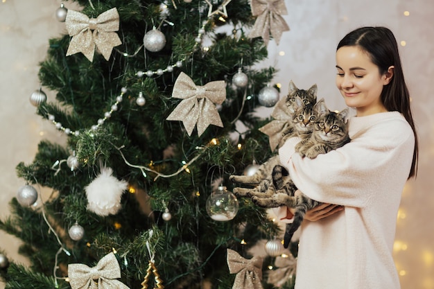 Niña sonriente con gatitos cerca del árbol de Navidad.