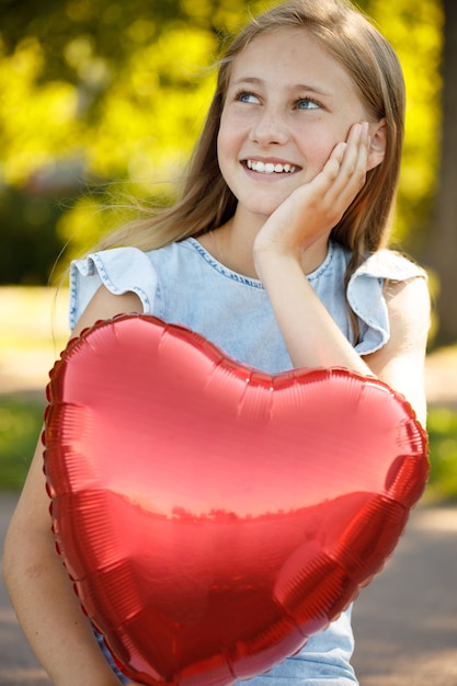 Niña sonriente con un globo en forma de corazón en la naturaleza