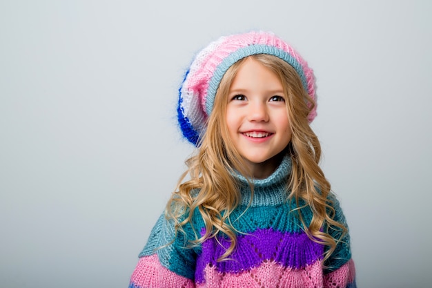 Niña sonriente en gorro de punto y suéter en aislante blanco