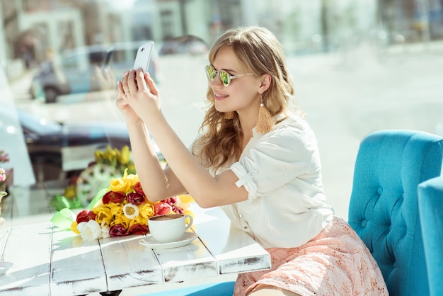 Niña sonriente hace un selfie sentado en la terraza del café