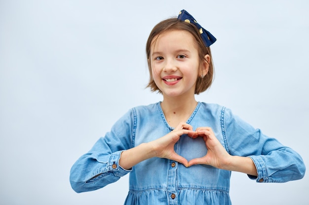 La niña sonriente hace el signo del corazón con las manos