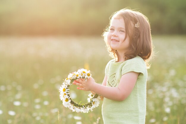 Niña sonriente haciendo guirnalda de flores posando en el campo