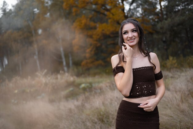 Niña sonriente con un hermoso vestido y peinado elegante en el bosque de otoño