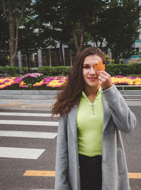 Foto niña sonriente con hoja de otoño en seúl