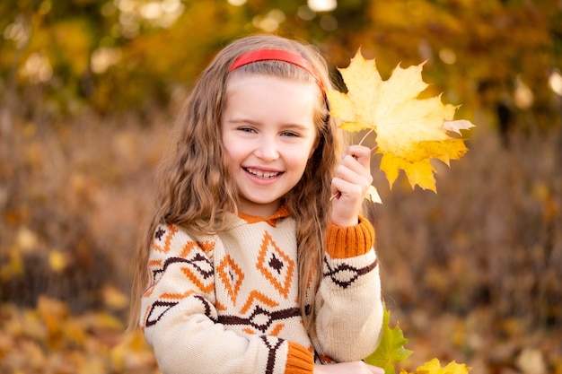 Niña sonriente con hojas de otoño en el parque