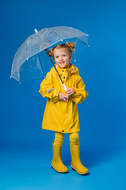 Niña sonriente en un impermeable amarillo y botas de goma con un paraguas