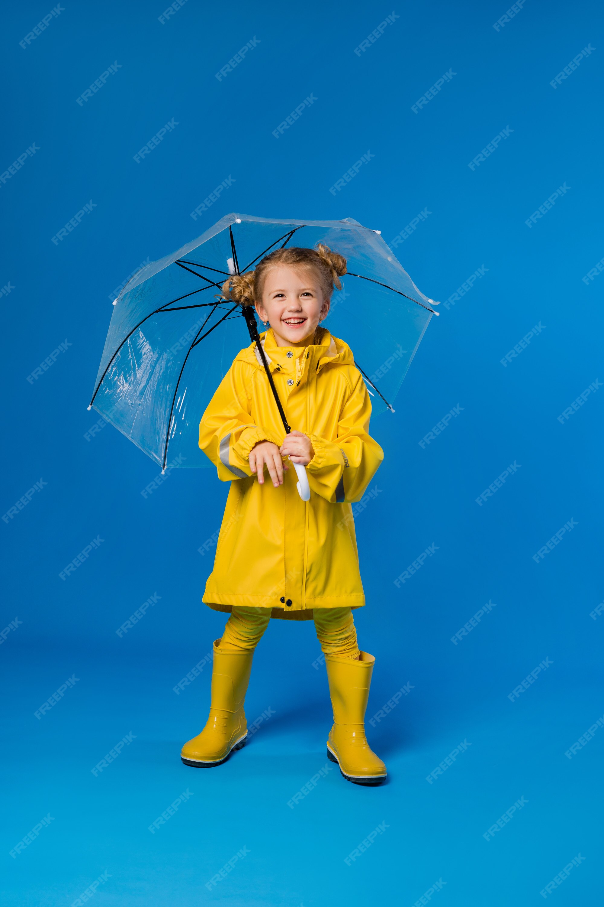 Niña sonriente en un impermeable y botas de goma un paraguas | Foto Premium