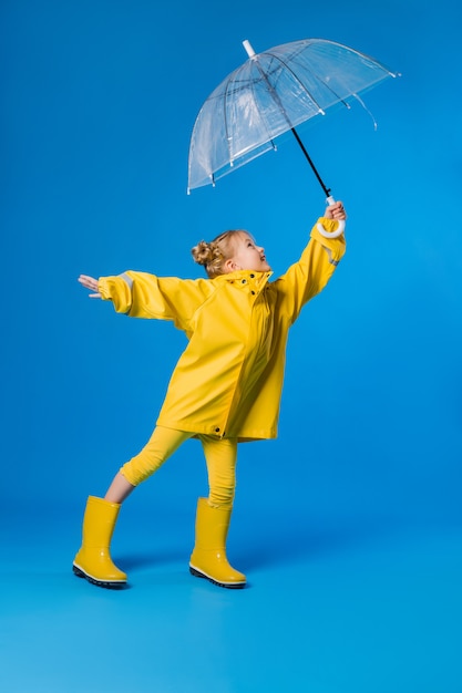 Foto niña sonriente en un impermeable amarillo y botas de goma con un paraguas