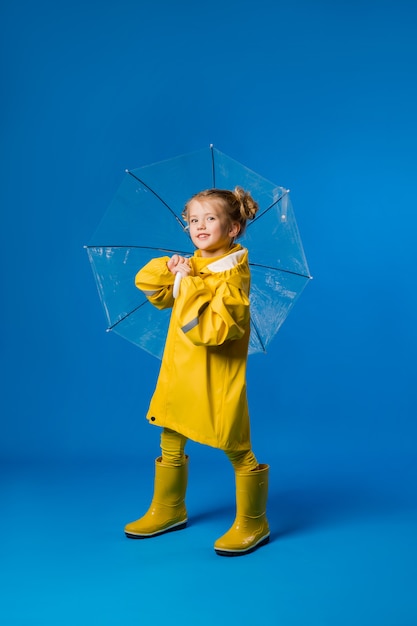 Niña sonriente en un impermeable amarillo y botas de goma con un paraguas