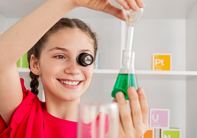 Niña sonriente con lente realizando un experimento químico