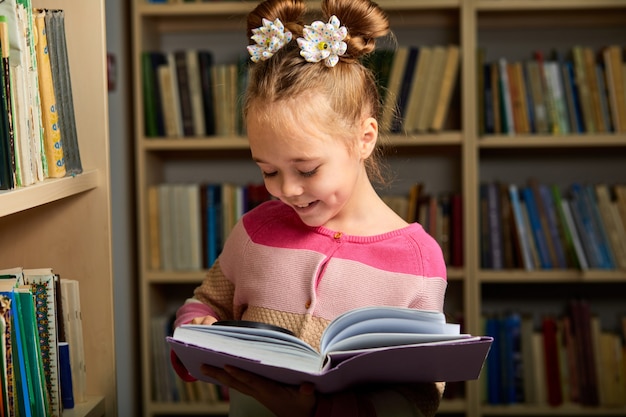 niña sonriente con lupa para leer mejor libros, ella disfruta de tiempo de educación, estudiando. en biblioteca