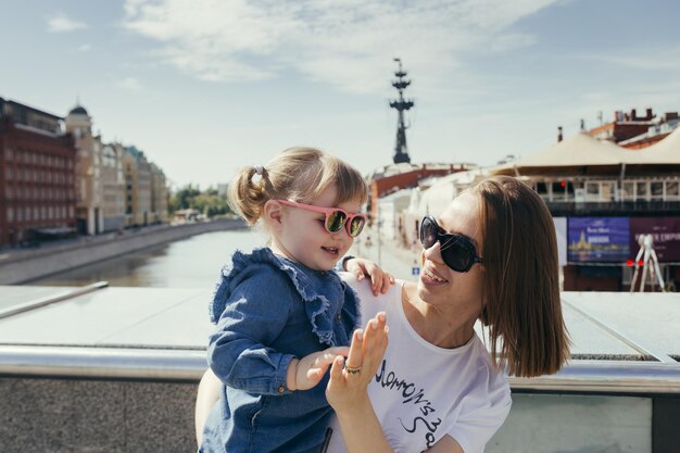 Foto niña sonriente y madre gestando en el puente sobre el río en la ciudad