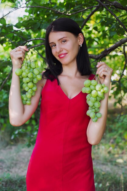 Niña sonriente mantenga pesados racimos de uvas, cosecha de otoño