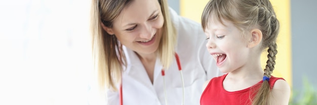 Niña sonriente con médico pediatra mira cápsulas transparentes. Recepción del concepto de complejos vitamínicos para niños.