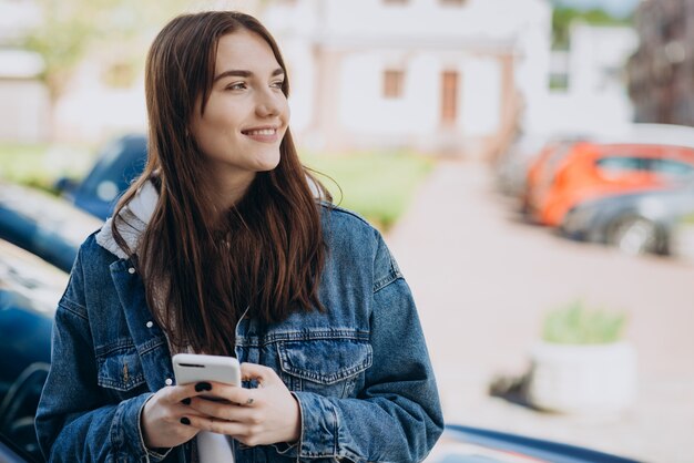 Niña sonriente en medio de la calle, sosteniendo un teléfono inteligente, mirando algo