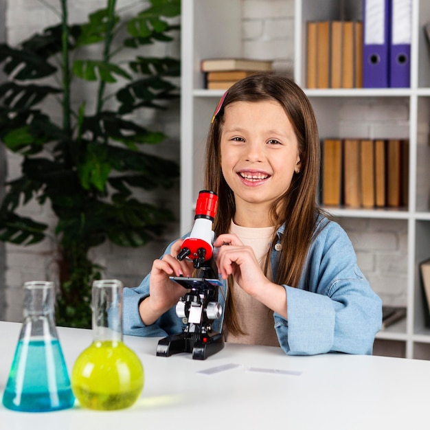 Niña sonriente con microscopio y tubos de ensayo