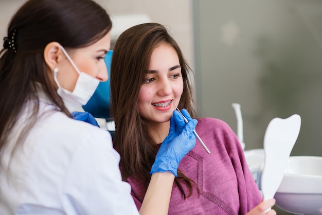 La niña sonriente se mira en el espejo para estimar el trabajo del dentista y disfruta del resultado con el especialista