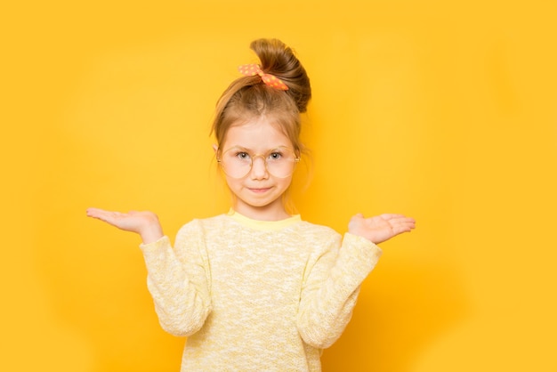 Niña sonriente muestra escalas en las manos en la pared amarilla. Copia espacio