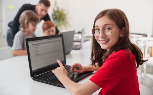 Foto niña sonriente navegando por ordenador portátil durante la lección de programación