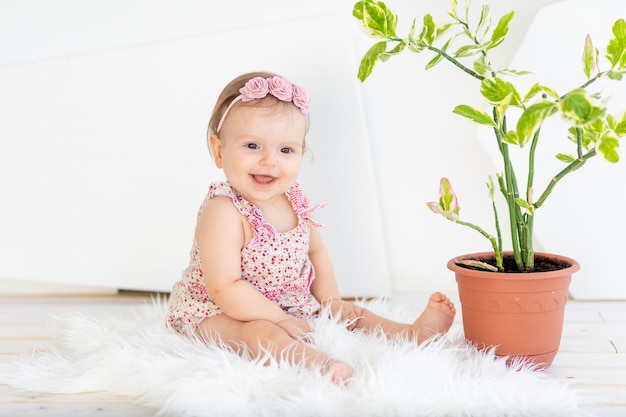 Niña sonriente niño sentado en una habitación blanca brillante con un vestido rojo con una flor de habitación