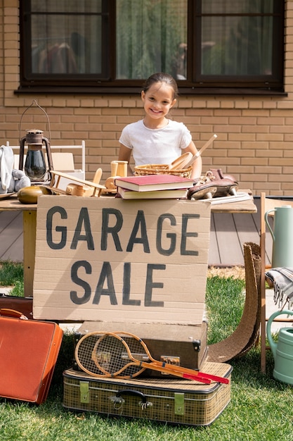 Niña sonriente ofreciendo cosas en venta de garaje