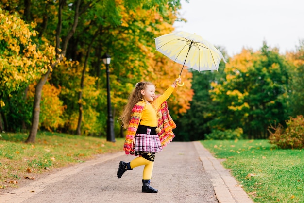 Niña sonriente con paraguas en un impermeable y botas al aire libre