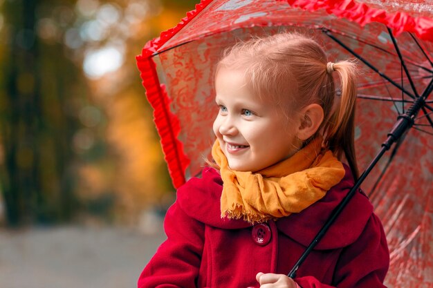 Niña sonriente con un paraguas en sus manos en el fondo del parque de otoño